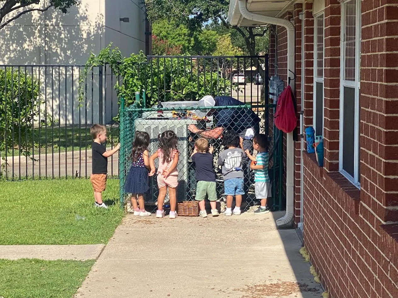 Anytime Heating & Air technician working on an outdoor AC unit while neighborhood kids watch