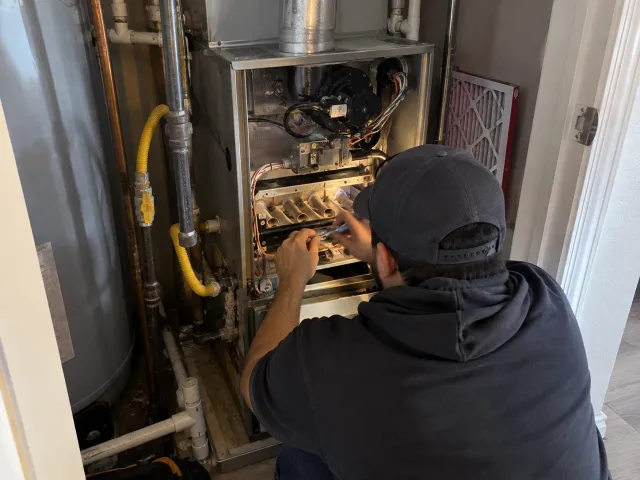 Technician repairing the burner assembly of a closet gas furnace beside a water heater