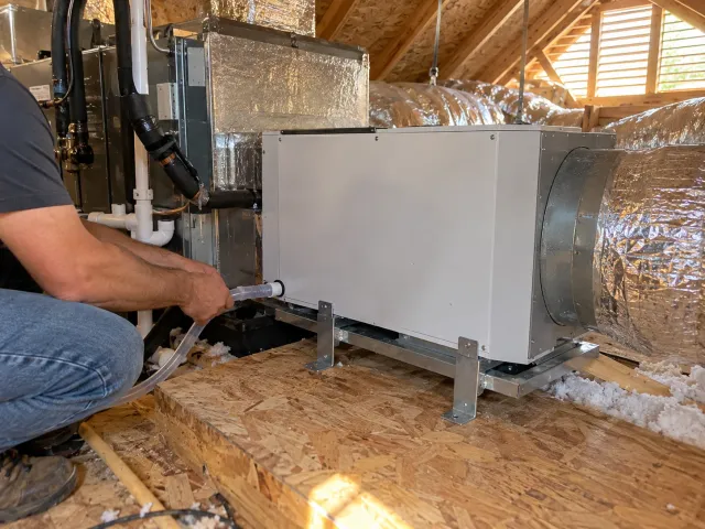 Technician connecting the condensate drain line on a whole-house dehumidifier in an attic